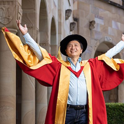 Li Cunxin AO stands in the Great Court wearing his red and yellow academic dress and cap.